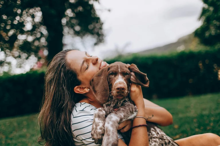 A woman hugs a German Shorthaired Pointer puppy while sitting outdoors on a grassy lawn.